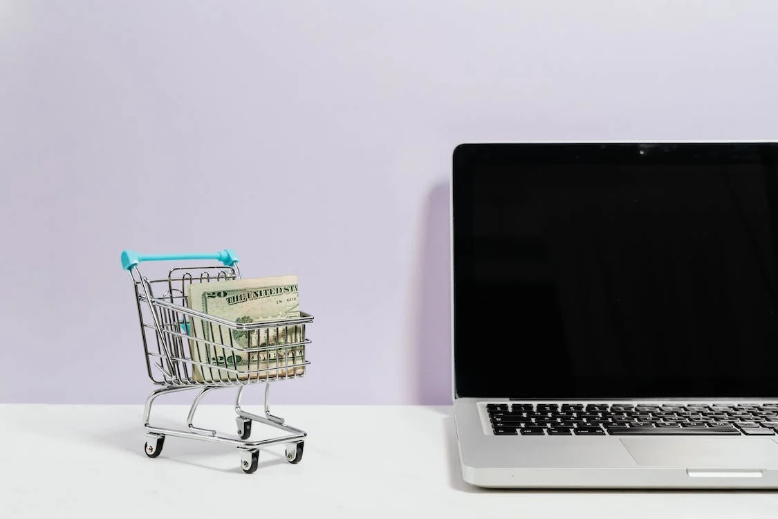 A miniature shopping cart next to a laptop.