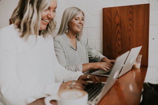 Two women smiling while looking at their laptops