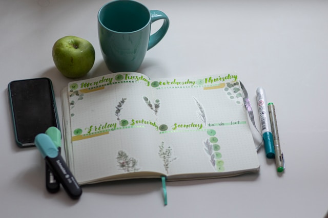 A mug, an apple, a phone, and pens next to a scheduling calendar
